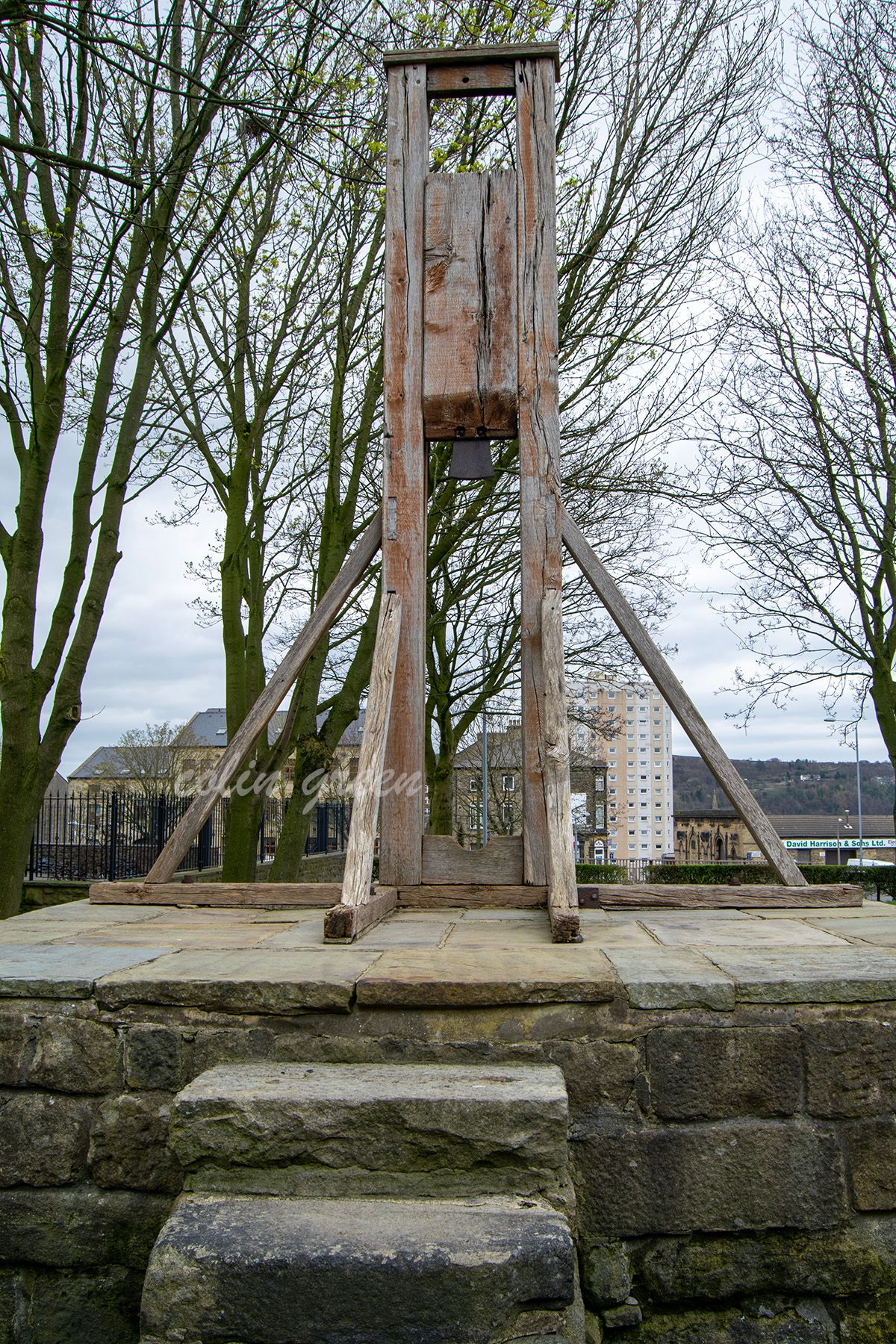 The Halifax Gibbet towering from it's base above the small park lined with trees.