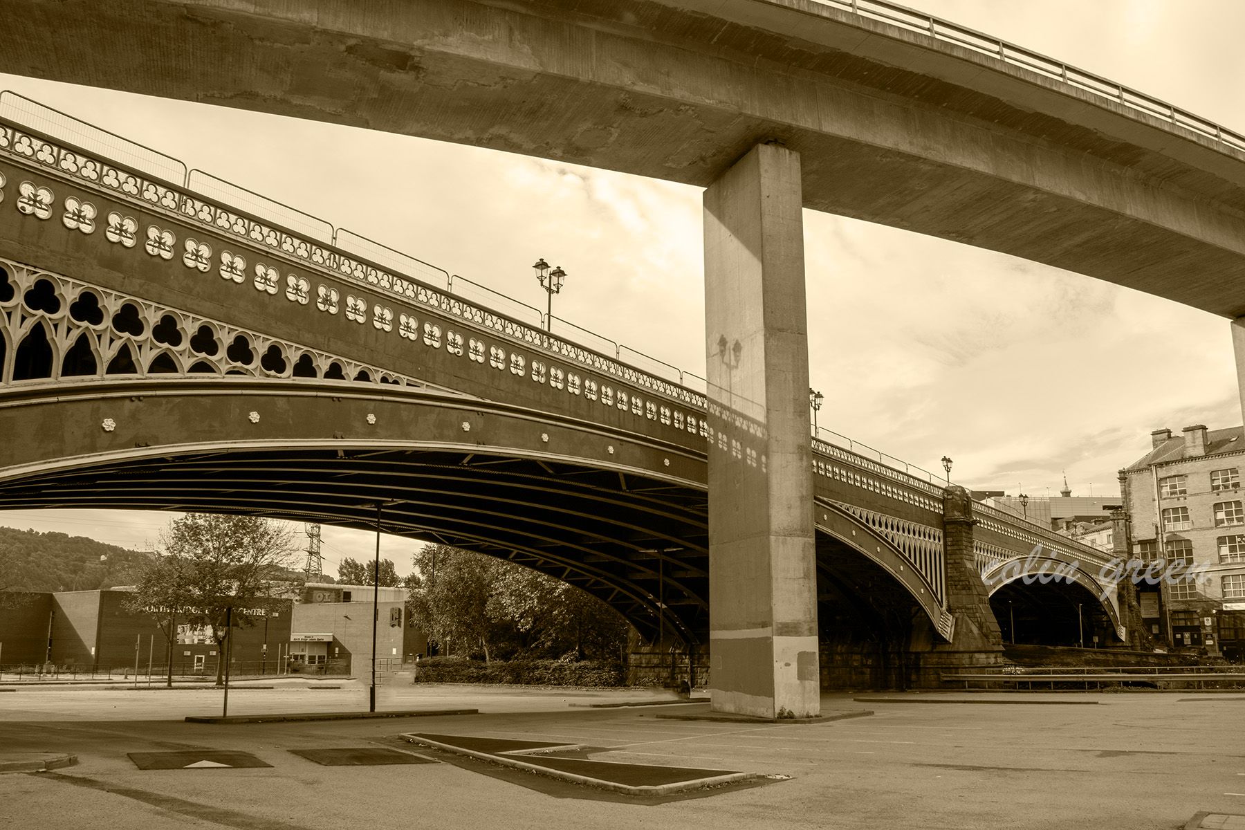 A sepia-toned photo of the North Bridge in Halifax, England. The old brick bridge with intricate arches is dwarfed by a modern concrete bridge above it