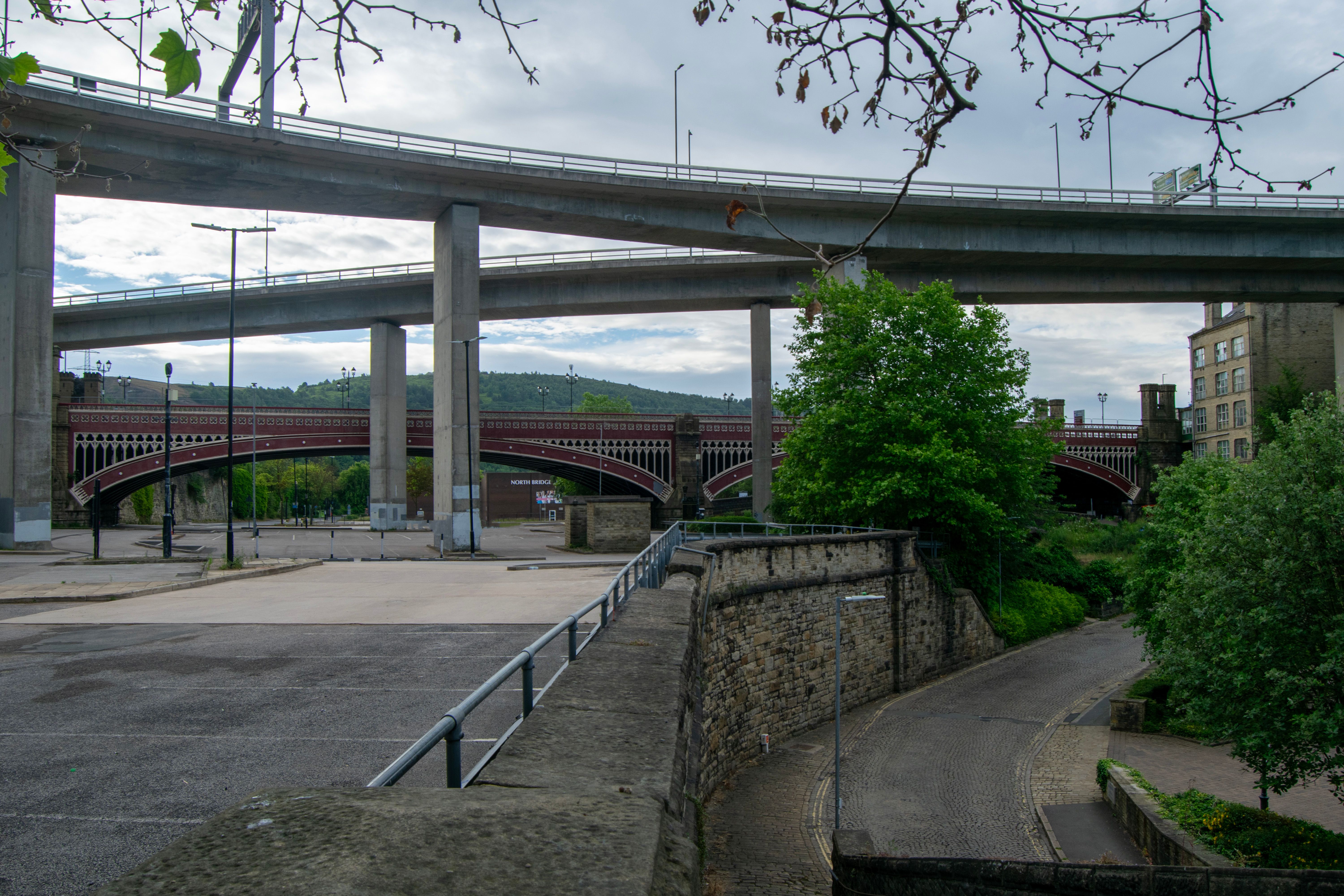 A view of the North Bridge in Halifax, England, with its distinctive red arches. A modern road bridge spans above it, showcasing the contrast between old and new infrastructure