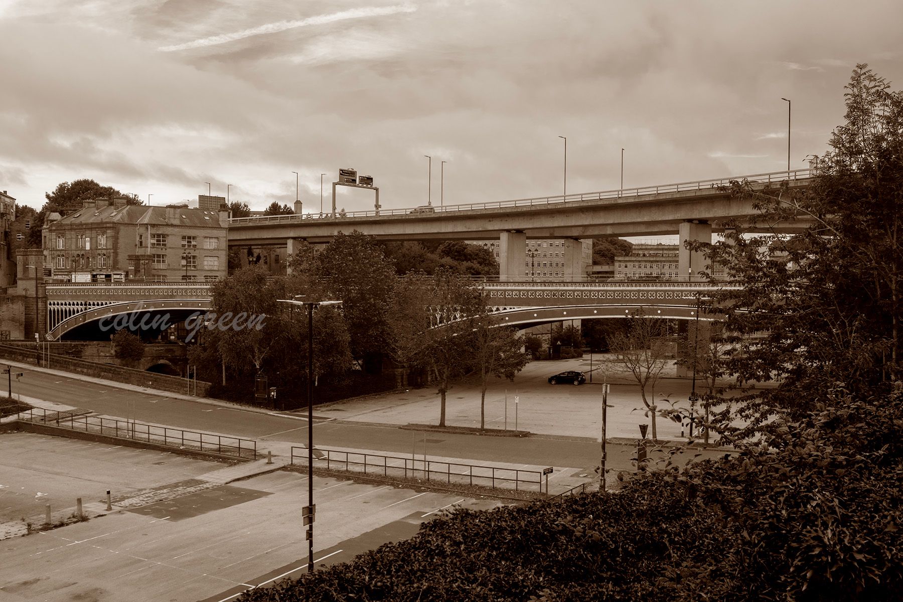 A sepia-toned view of the North Bridge in Halifax, England. The old brick bridge with intricate arches is dwarfed by a modern concrete bridge above it, symbolizing the passage of time and changing infrastructure