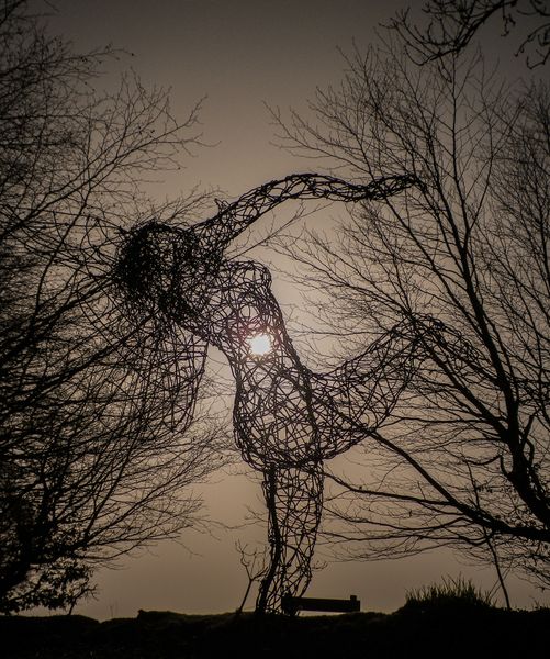 Silhouette of dancing wire fairy figure against the sun and merging with tree branches